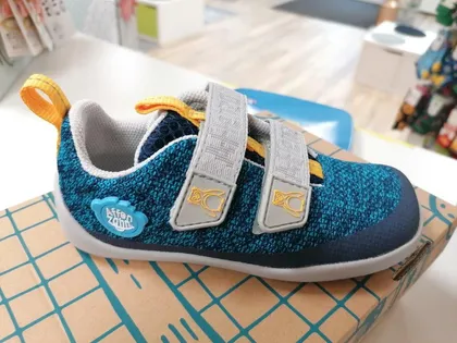 Blauer Strick-Klettschuh mit gelben Laschen auf einem Schuhkarton