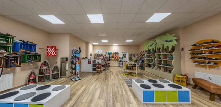 Verkaufsraum mit bunten Sitzinseln zum Anprobieren, Schuhregalen an den Wänden und einer Turnbank